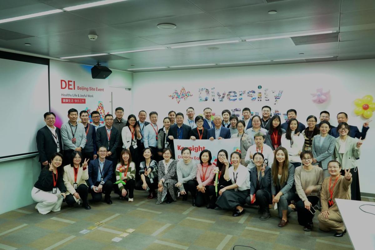 A large group photo of people stood in front of the Diversity Equity Inclusion wall display 