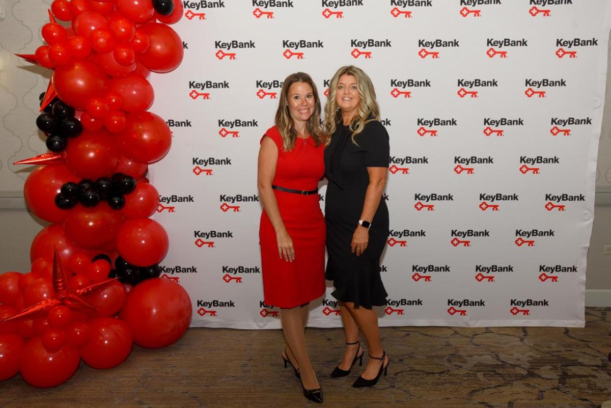 Two people standing together next to a column of red and black balloons, with a KeyBank backdrop