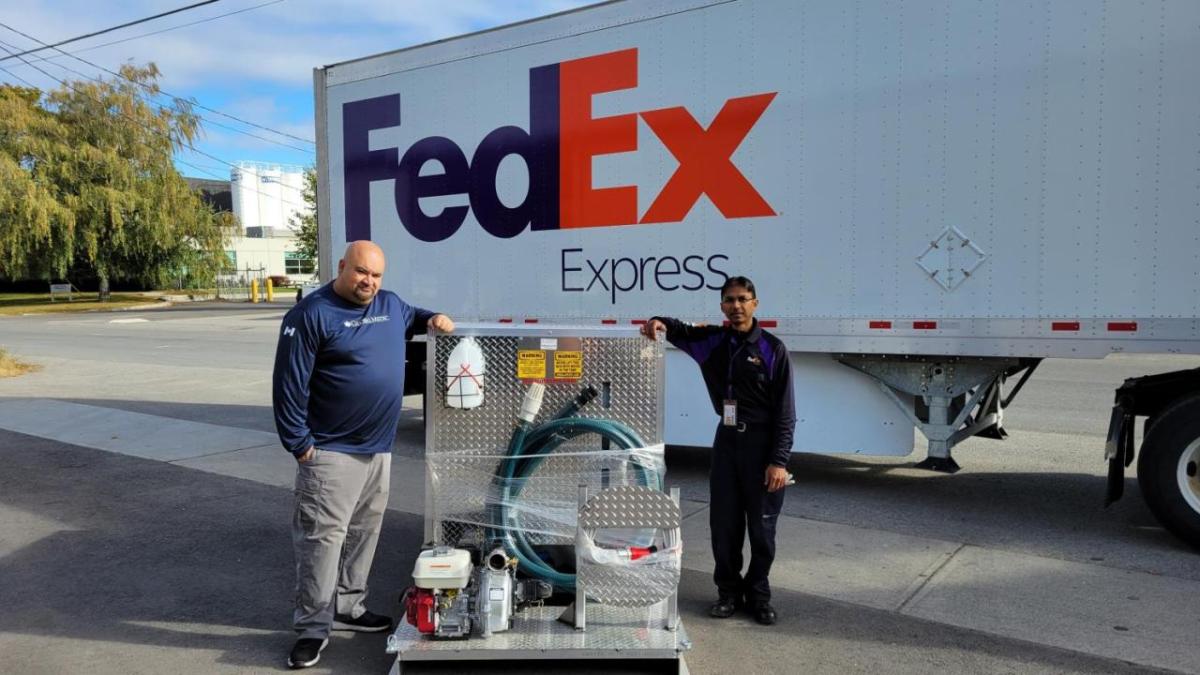 Two people standing next to a FedEx truck with a delivery of equipment