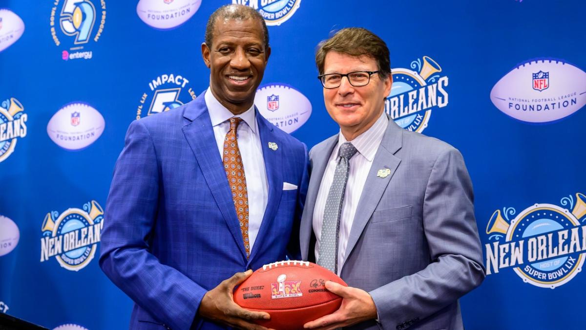 Two people in suits holding the same football and smiling