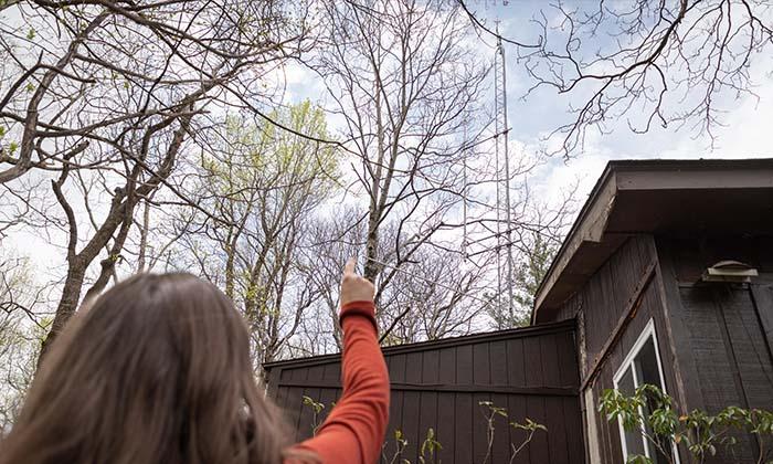 Jennifer McCarthey Tyrrell pointing at a Motus tower atop a brown building