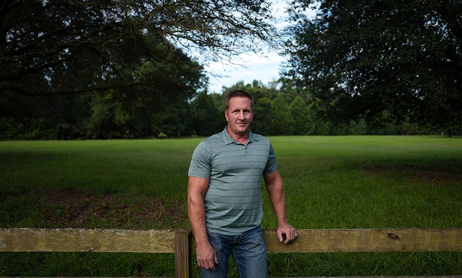 Slade Williams in a green shirt standing in front of a stockade fence