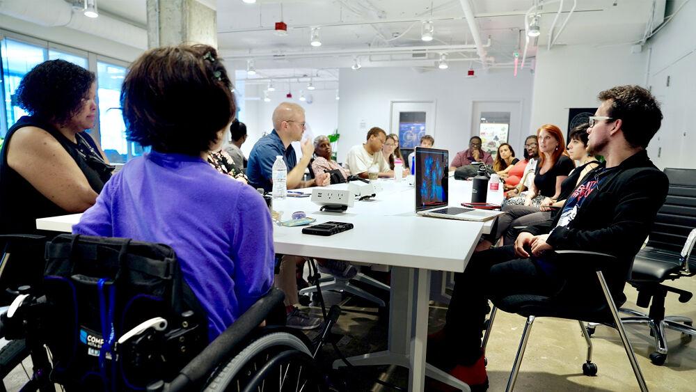 A long table with seated people around it. Some with open electronic devices.