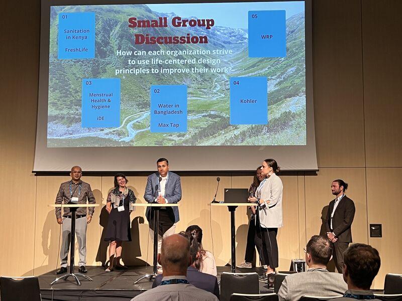 People on a stage underneath a screen that says Small Group Discussion