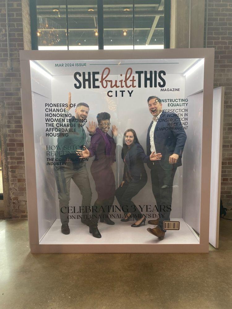 Four people posing inside a glass box decorated as if on a magazine cover