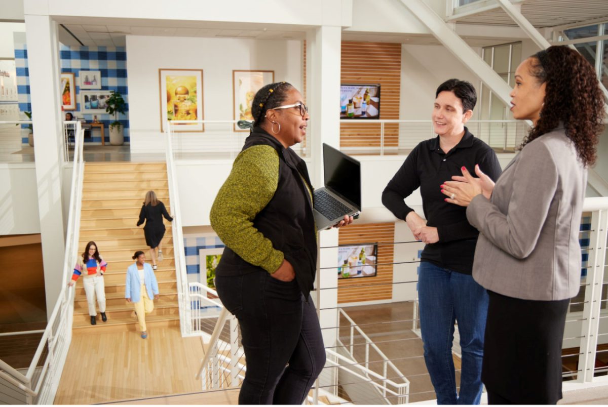 Three Bath & Body Works associates stand together at the top of a staircase talking at the company’s headquarters in Columbus, Ohio.  