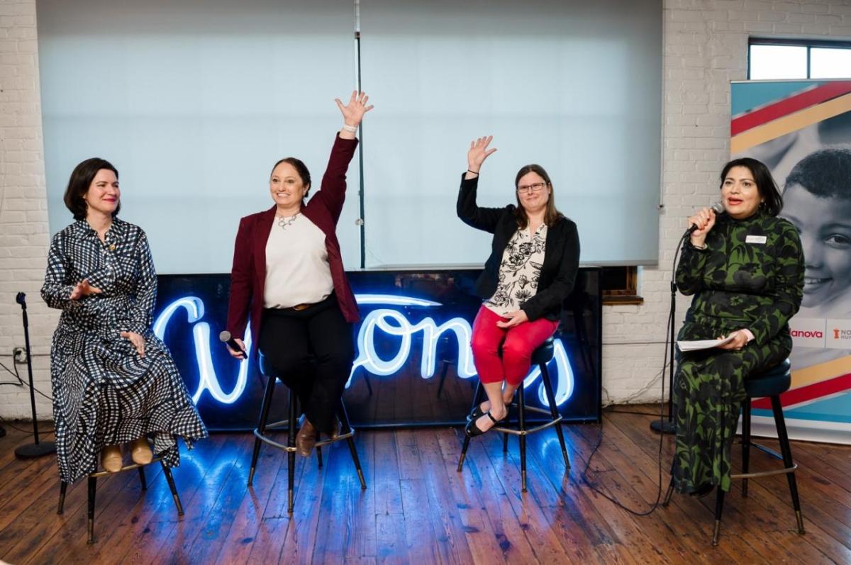 A group of women sitting on stools with their hands up