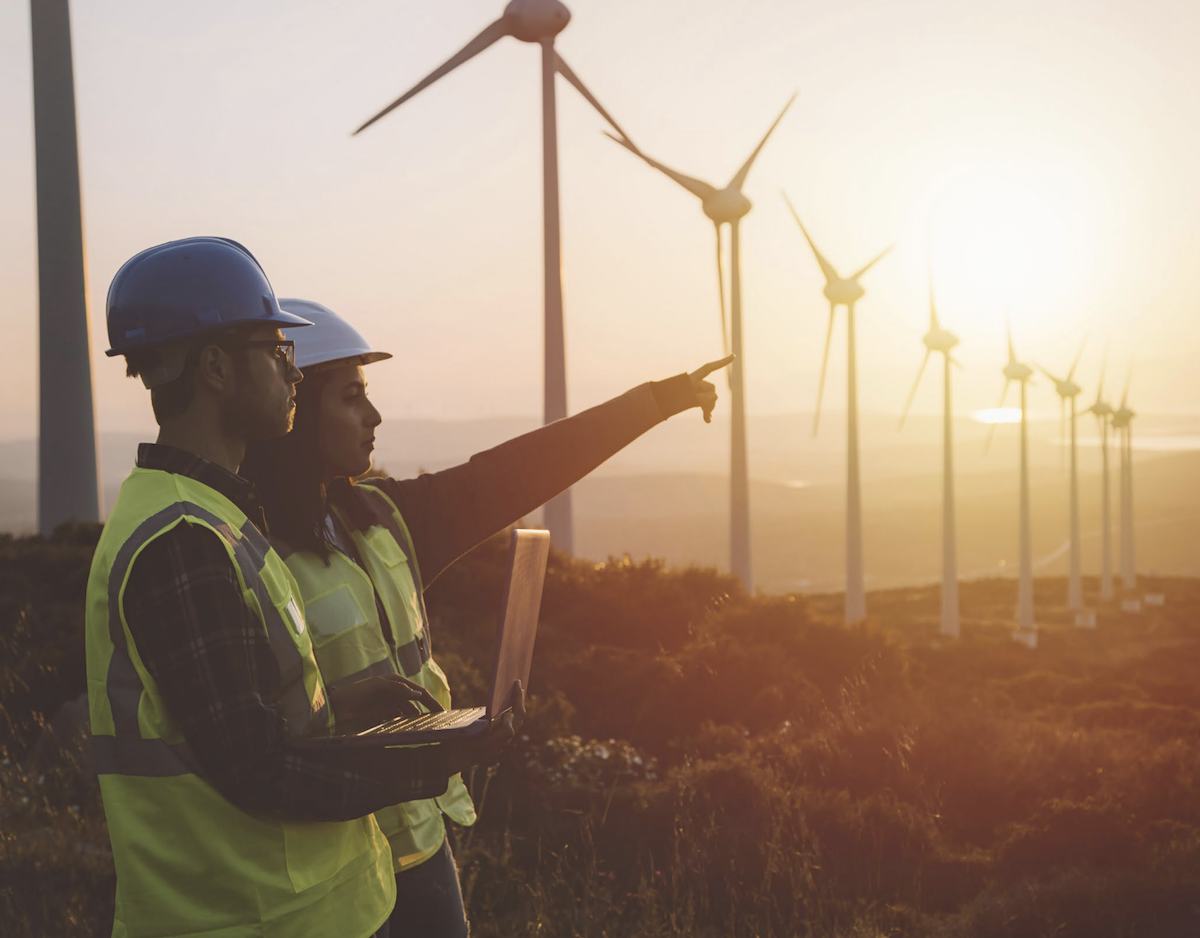 Two team members in a field with windmills at sunset.