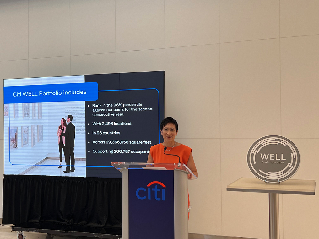 A person behind a podium speaking, with a screen behind them