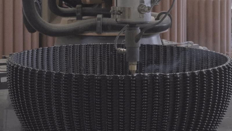 3D printer creating a piece of furniture with hot, black liquid material.