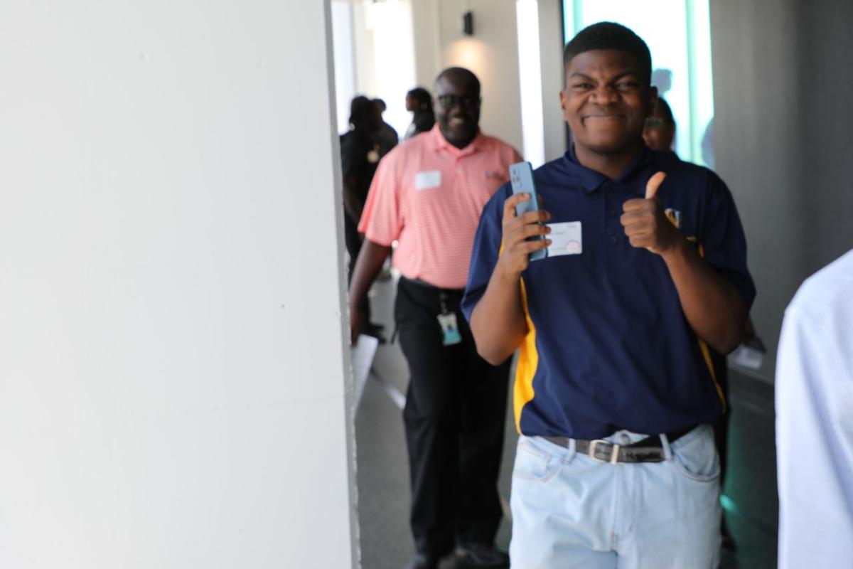 People walking through a corridor, one person smiling at the camera with their thumbs up