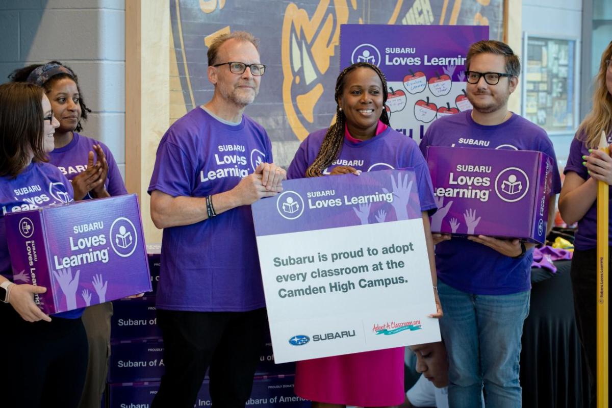 A group of people wearing purple t-shirts and holding Subaru loves learning boxes