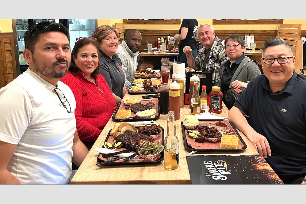 People smiling, sitting at a dining table with food in front of them