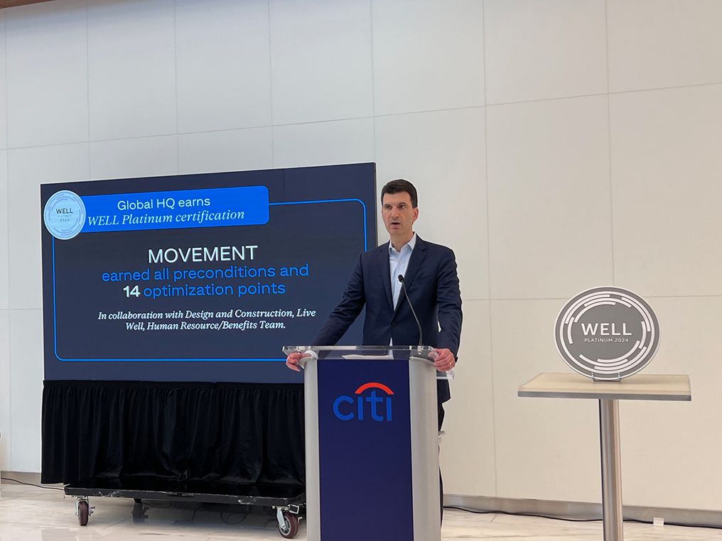 A person behind a podium speaking, with a screen behind them