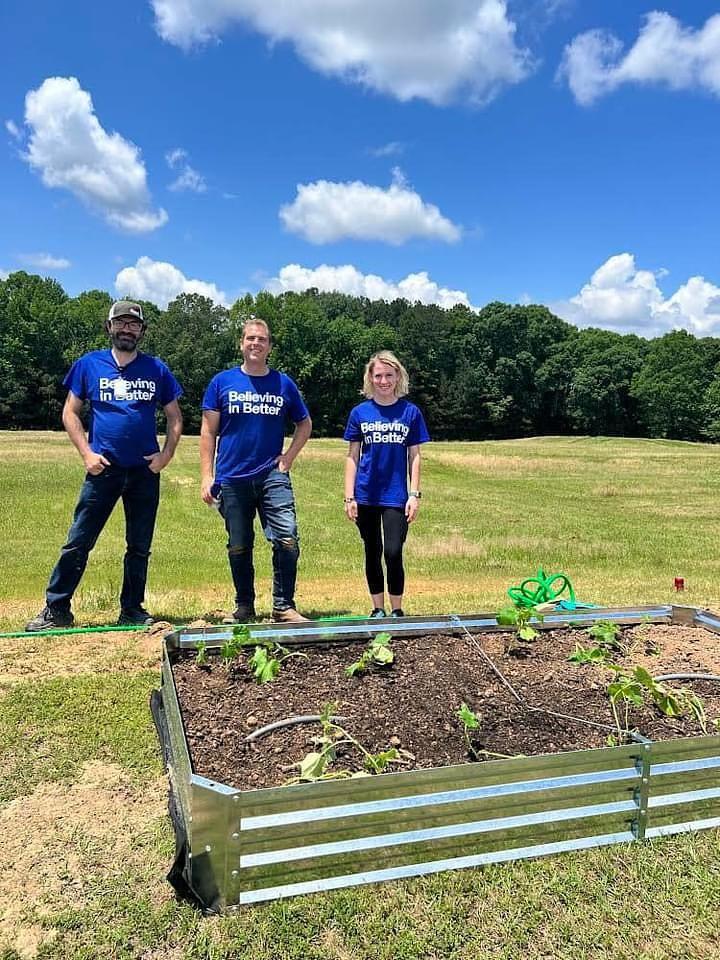 Three people stood behind a raised bed in a field for planting fruit and veg