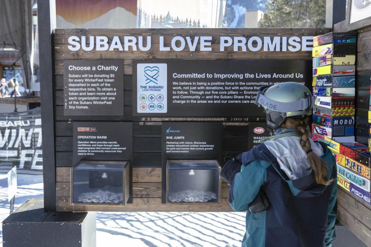 A person in a ski helmet reading a board that says "Subaru Love Promise"