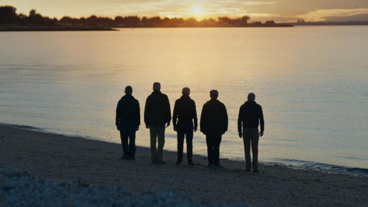 Five people stood on a beach watching the sunset 