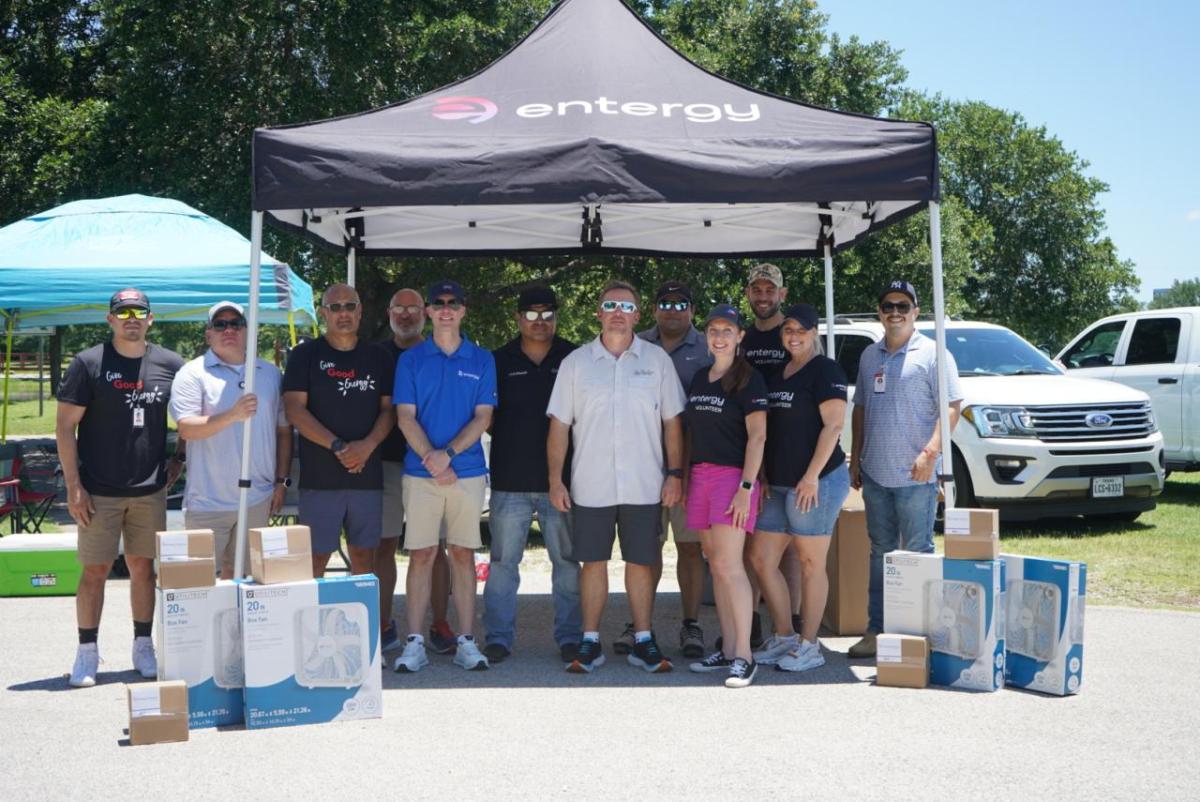 People standing together outside under an Entergy tent, with boxes of new fans