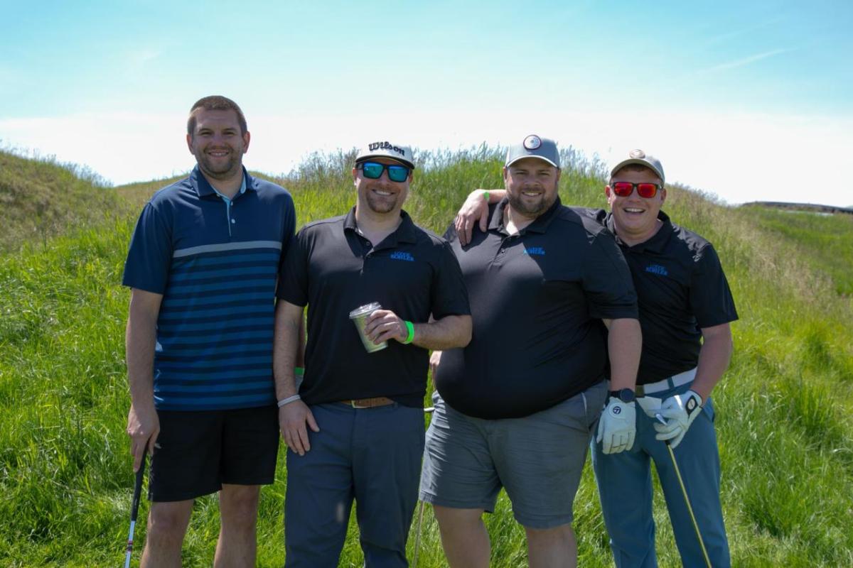 Four people standing together outside on a grassy area