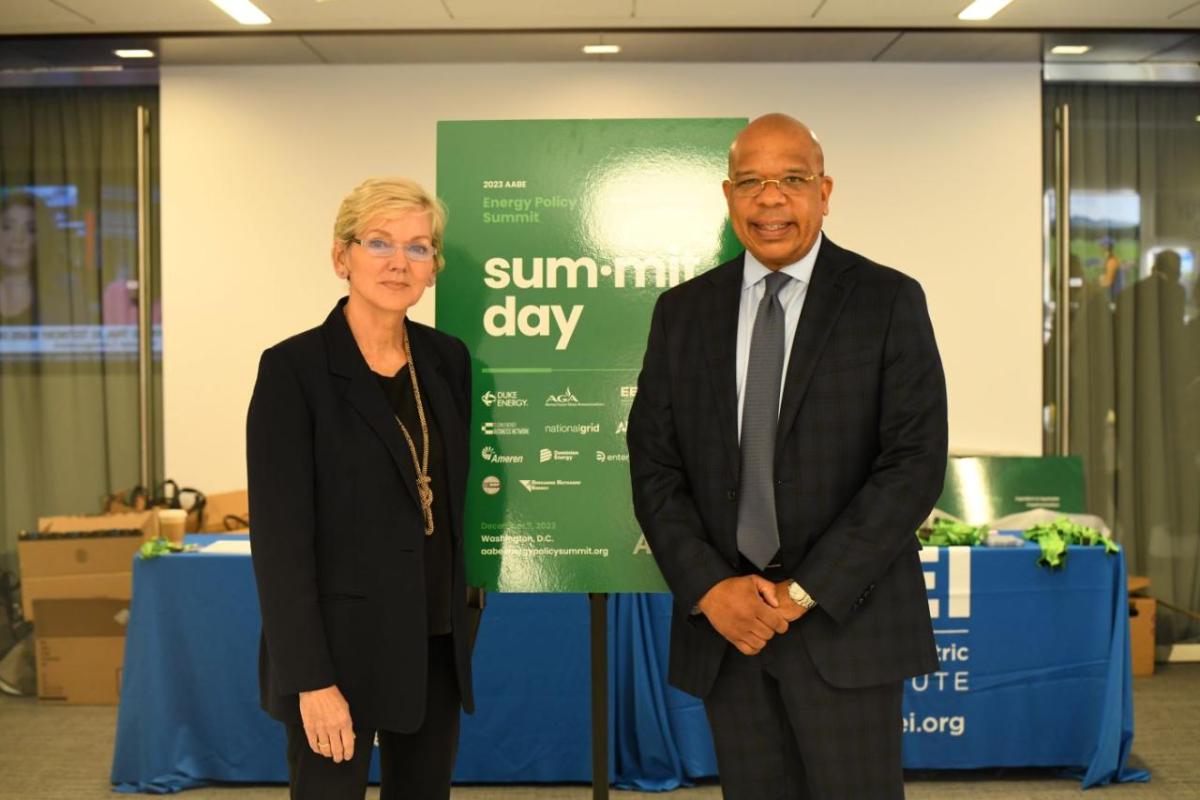 2 people in front of AABE Energy Policy Summit poster