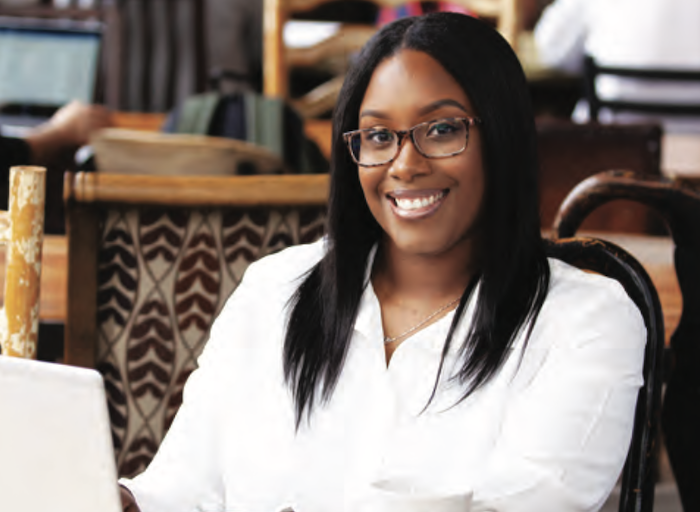 African American female, smiling, at work behind a laptop.