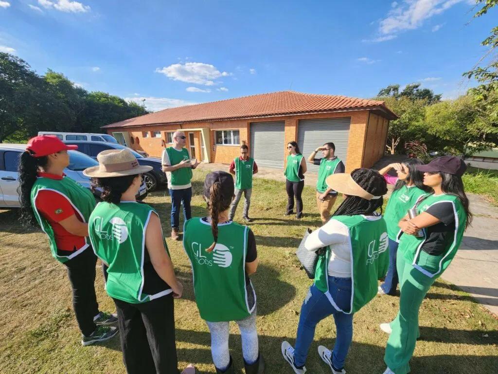 Students and adults in matching green vests meet in a circle outside a building in a rural area.