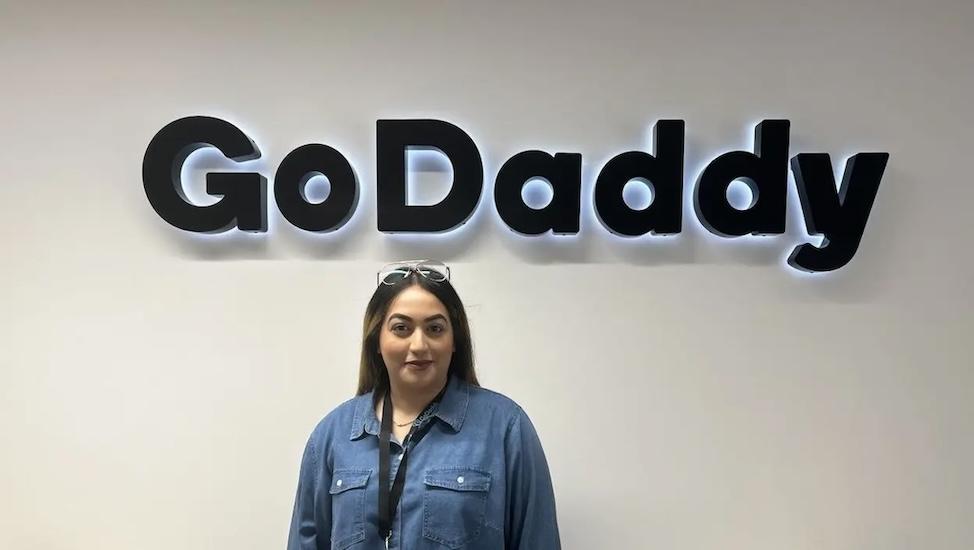 Aisha shown underneath a GoDaddy sign at work.