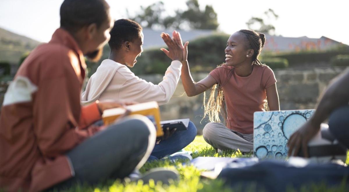 Photo of two students high fiving while sitting on the grass