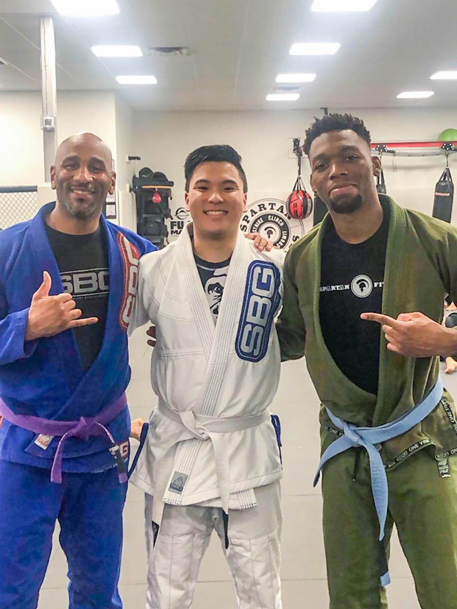 Three people wearing martial arts suits with their arms around each other