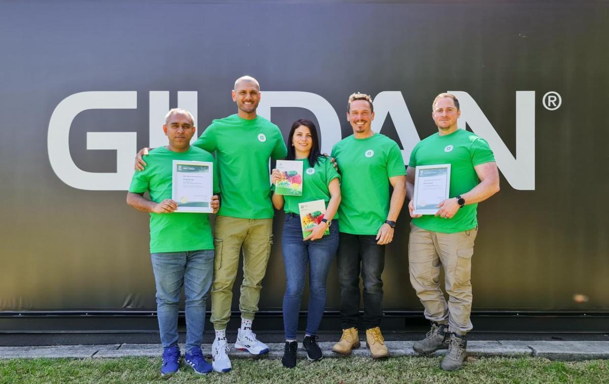 Five mental health first aid certified employees from Gildan Australia posing with their certificates in front of a Gildan logo