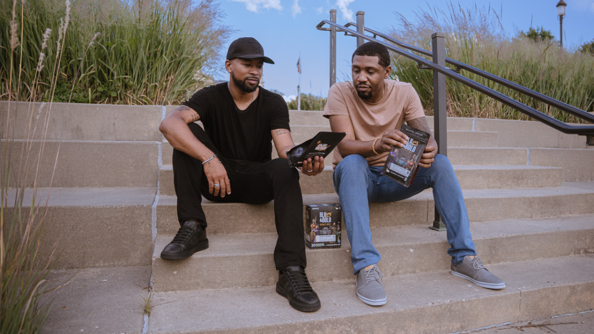 2 men sit on stairs viewing bags of BLK & Bold Coffee