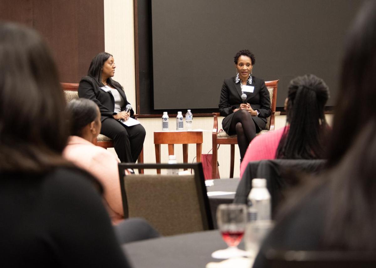 Two speakers seated on a stage in front of a room of others