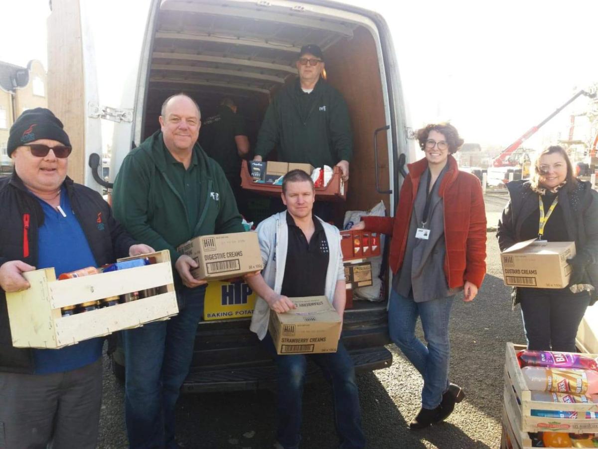 A group of six people carrying boxes, smiling at the camera. An open truck behind them with a person inside.