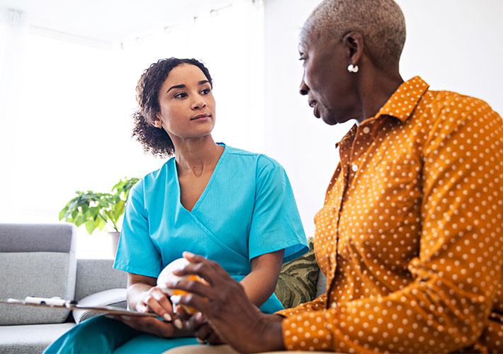 A person in scrubs and a patient sitting next to each other, looking at the other.