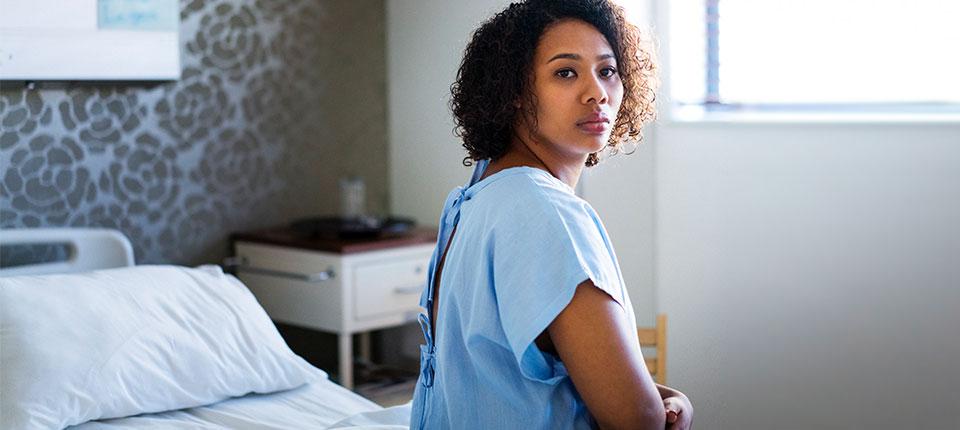 Patient in hospital gown sitting on a bed, turning to look behind her