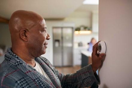 A person in a robe adjusting a thermostat in a home setting.