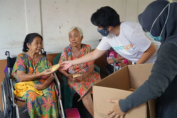 Two volunteers handing out food to two elderly people in chairs