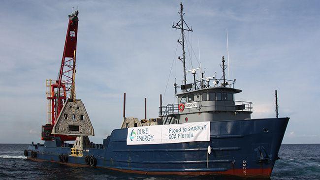 large boat in open water, a crane in back lifts a cement structure. Duke Energy banner hangs on the side of the boat