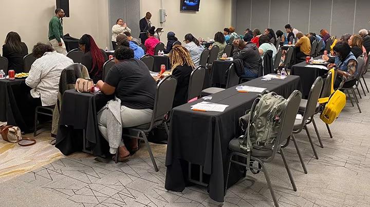 People sat at rows of tables and chairs at an event 