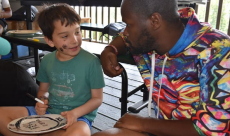 An adult talking with a smiling child who is drawing.