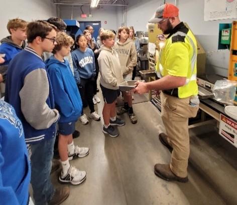 A volunteer in safety uniform showing something to a group of kids.