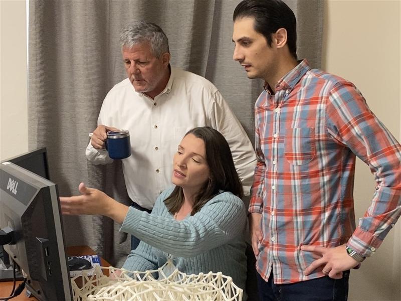 Carolyn Woeber sitting at computer with 2 men standing behind her