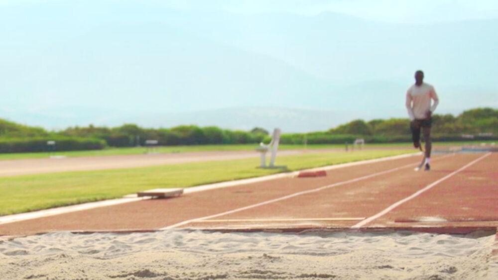 A person running from a distance on a track towards a sandy area.