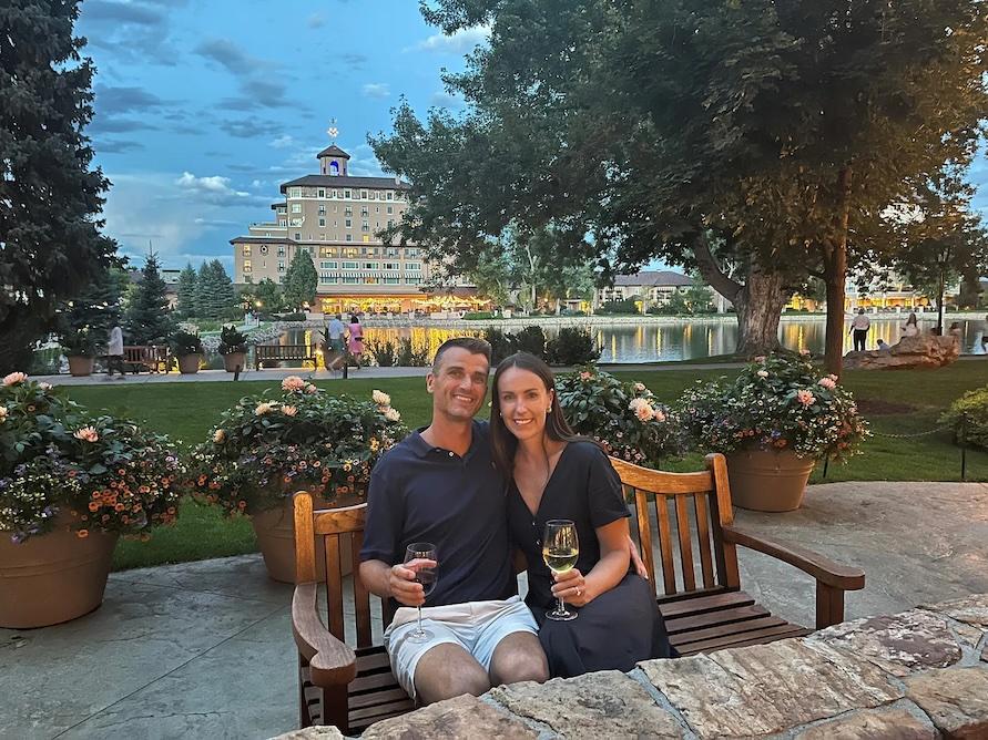 Christine Perkins and her husband seated in a beautiful garden holding a glass of wine.