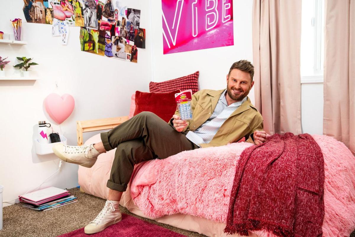 3M Director of dorm design, Bobby Berk, shown sitting on a bed.