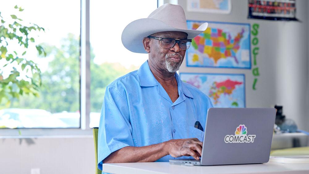 A seated person using a laptop computer with Comcast logo on it in a classroom setting.