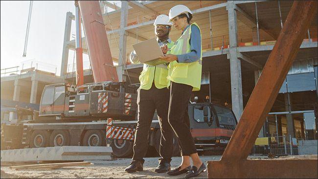 Two people looking at a laptop on a construction site.