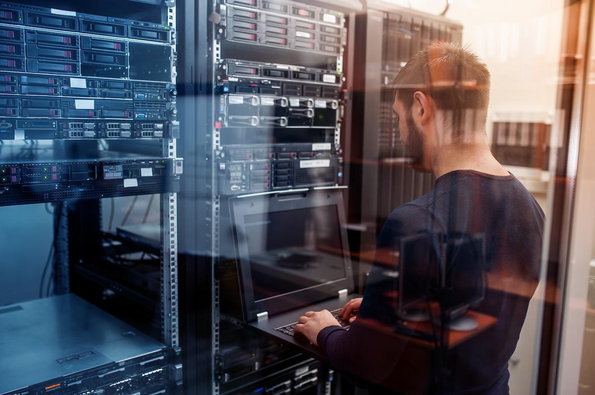 Tech working on a laptop in a server room.