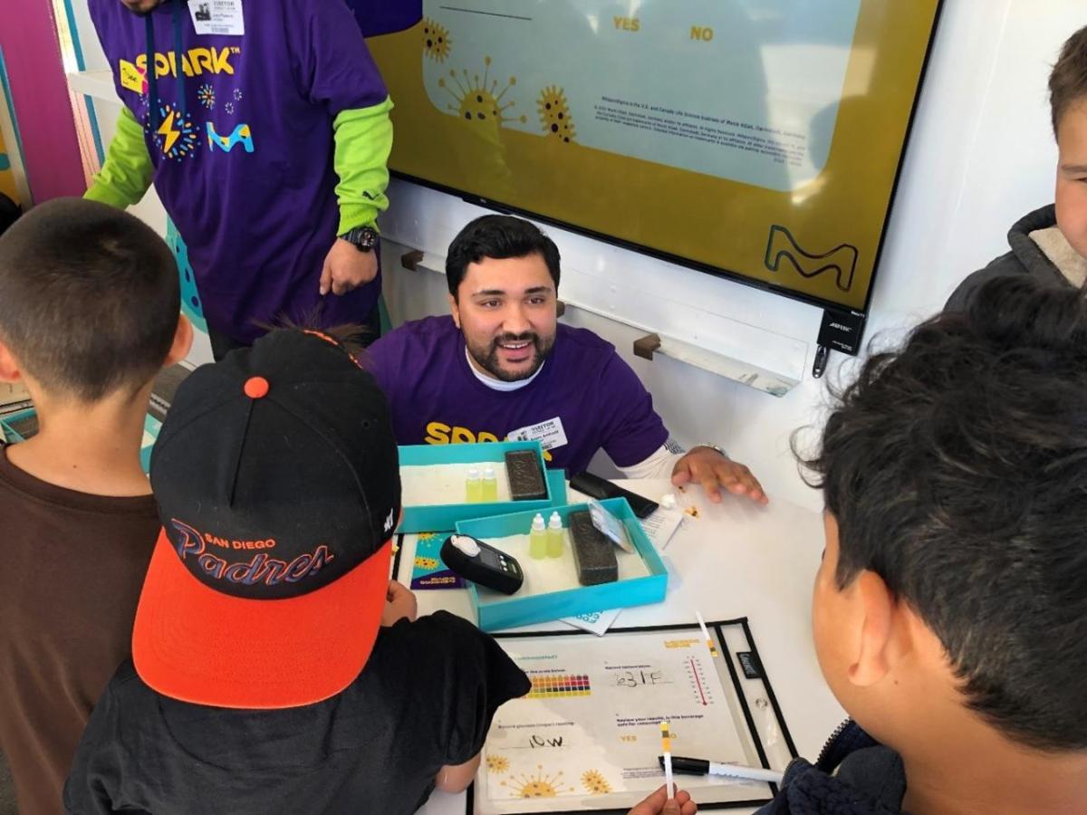 A SPARK employee kneels down over an experiment to talk to students. 