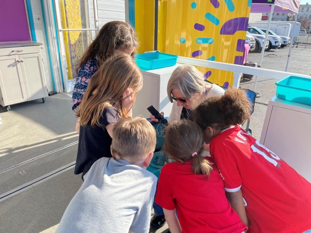 A woman is sitting while a group of students look over her at an experiment. 